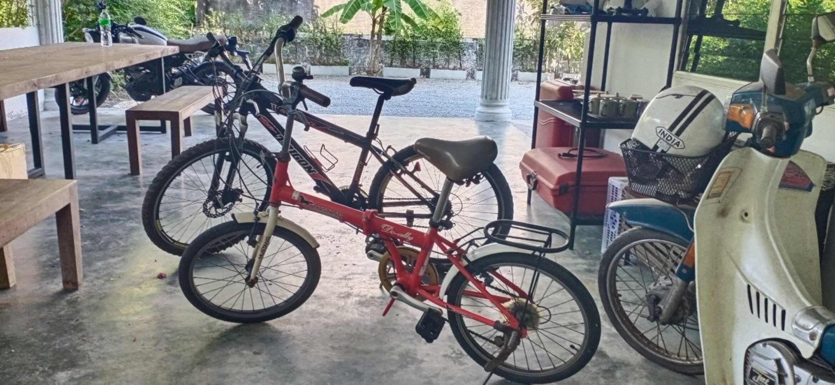 A bicycle and a scooter in a covered outdoor area with tables and chairs.