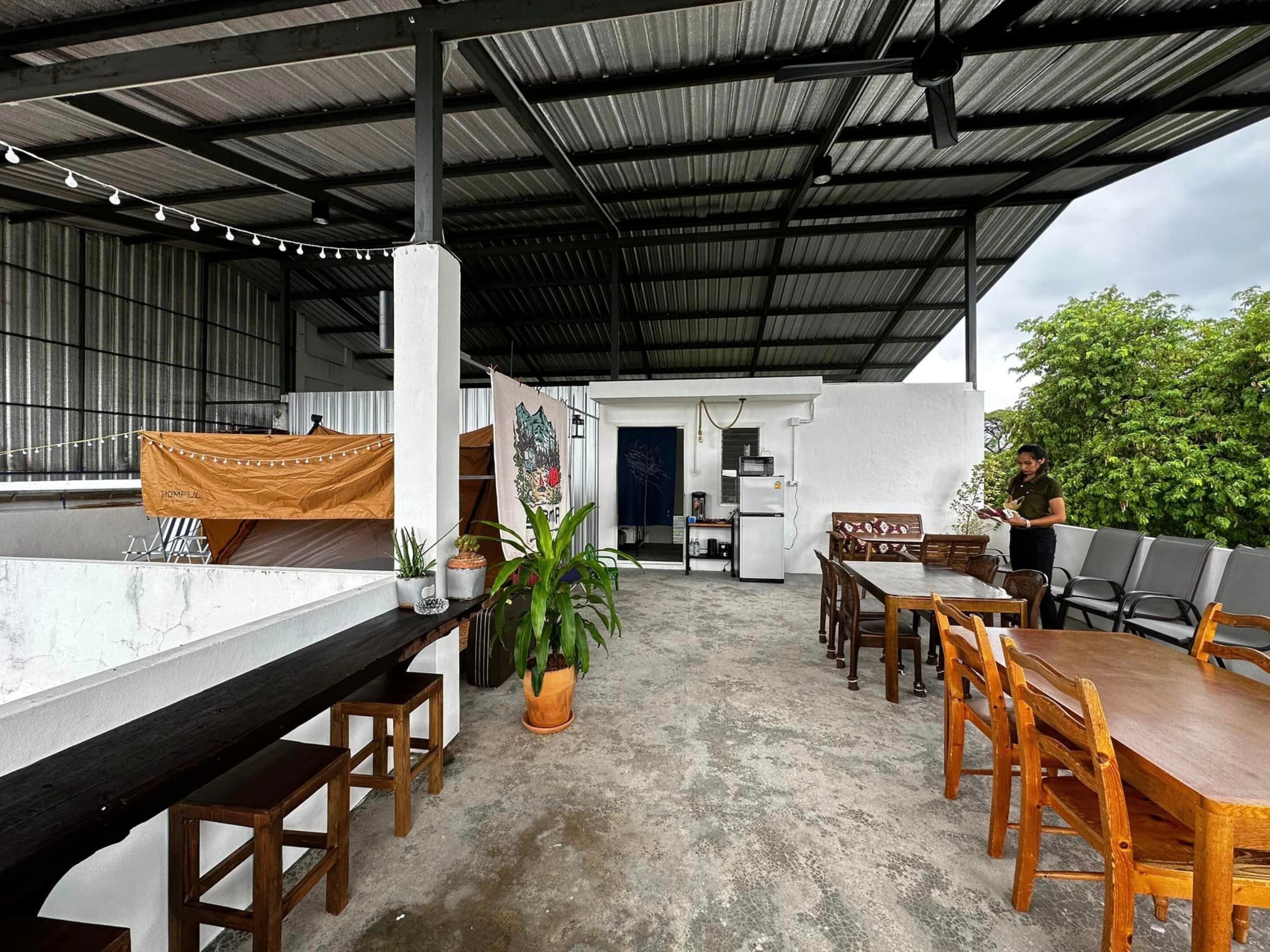 Ein Patio im Freien mit einem langen Holztisch und Stühlen, einer kleinen Küchenzeile mit Kühlschrank sowie einer Sitzecke mit Stühlen und Tisch.
