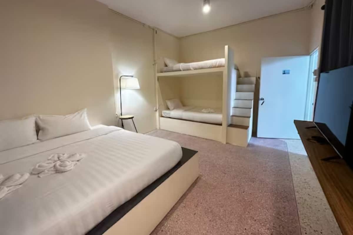 Habitación de hotel con una cama grande, una lámpara de noche, una cama litera y una puerta que da a otra habitación.