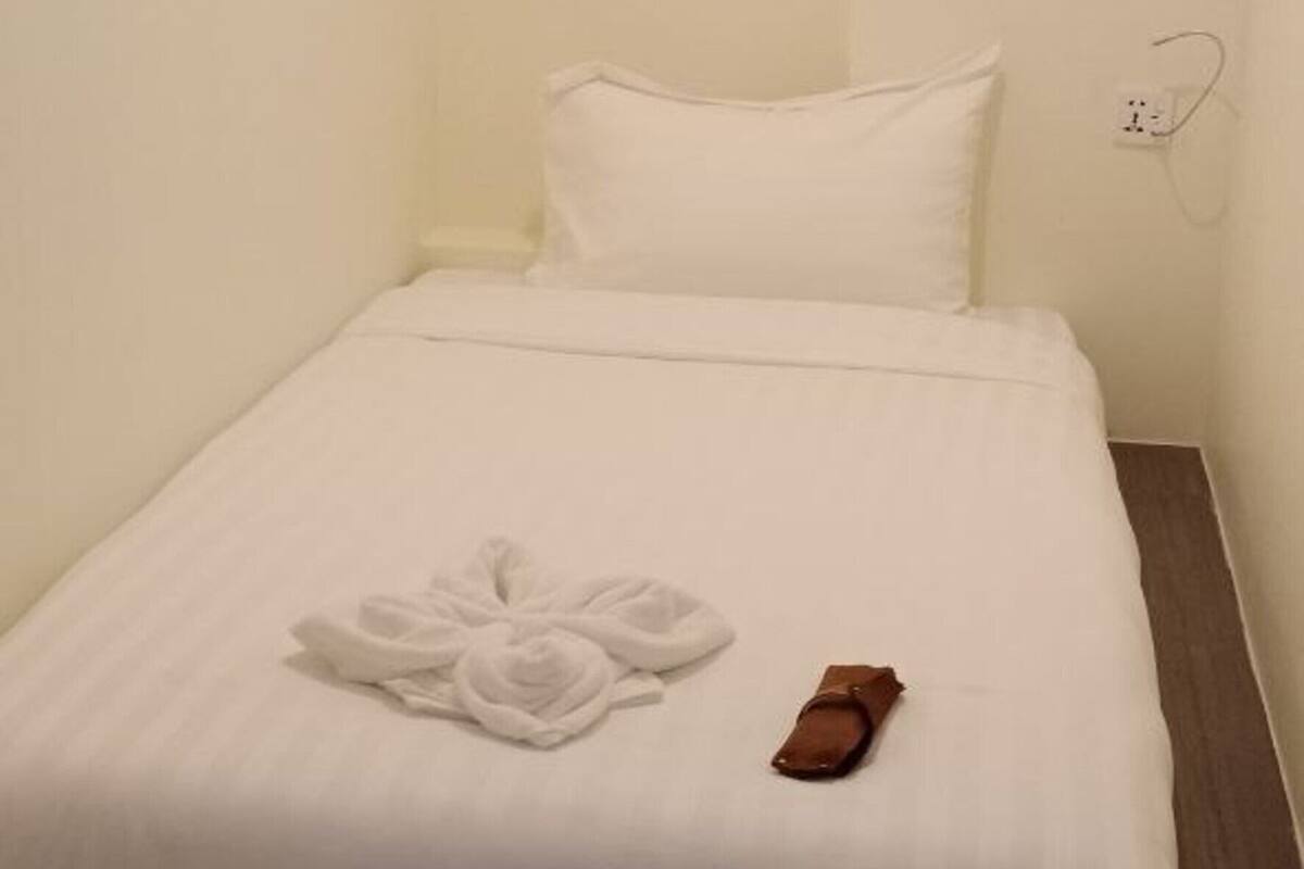 Una cama bien hecha con edredón blanco y una toalla con diseño de rosa, un objeto marrón sobre la cama y un enchufe en la pared.