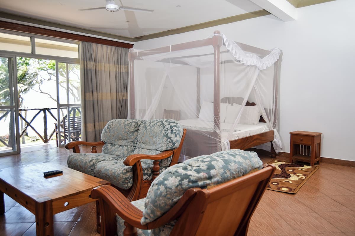 Una habitación con una cama de madera, una mesa de madera y dos sillones tapizados.