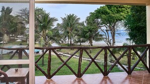 A balcony with a wooden railing, a view of a beach, palm trees, and a pool area. - Coral Beach Resort (Diani Beach)