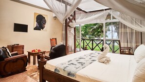 A bedroom with a bed, a wooden chair, a small table, and a TV. - Coral Beach Resort (Diani Beach)