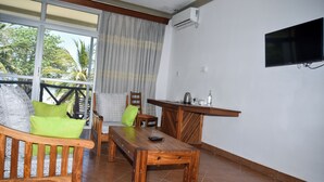 A wooden dining table with chairs, a sofa with cushions, a small kitchen area with a sink and countertop, and a TV mounted on the wall. - Coral Beach Resort (Diani Beach)