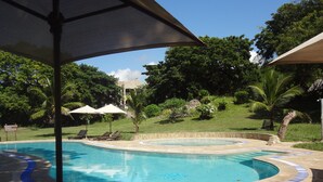 A swimming pool with lounge chairs and umbrellas, surrounded by greenery and a building in the background. - Coral Beach Resort (Diani Beach)
