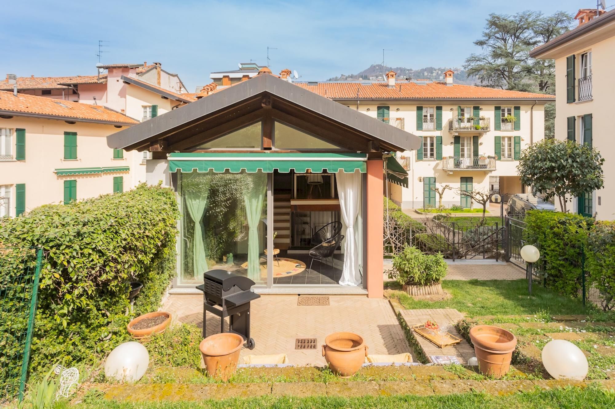 A small outdoor seating area with a grill, surrounded by terracotta pots and a green awning.