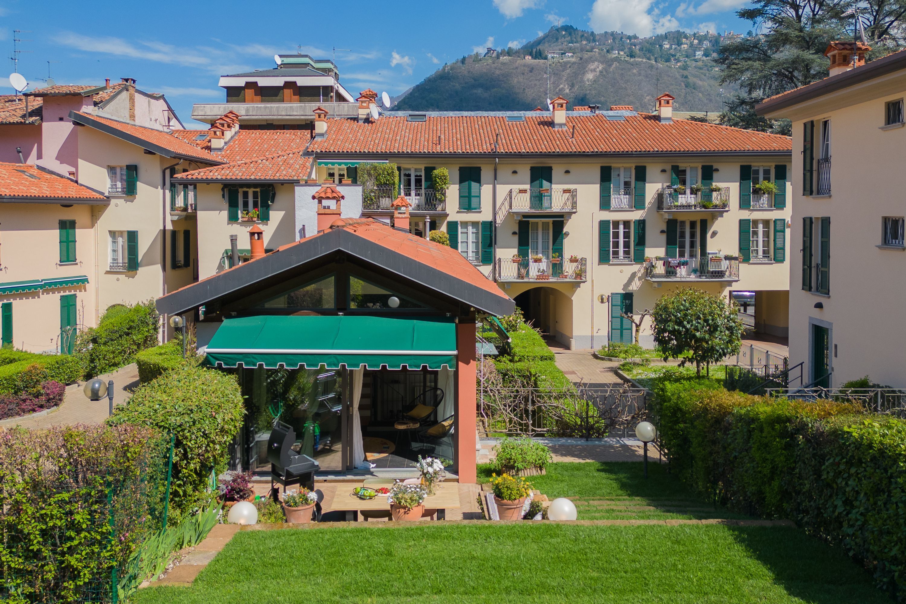 A courtyard with a covered seating area, surrounded by buildings with red-tiled roofs and green shutters.