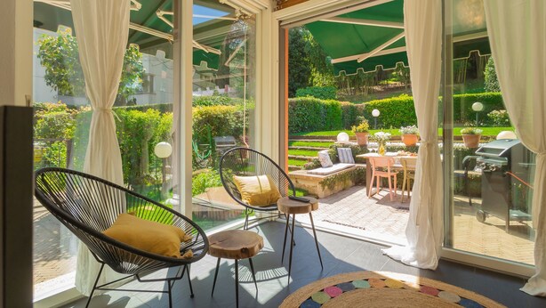 Un patio soleado con zona de comedor, una parrilla y vistas a un jardín cuidado.