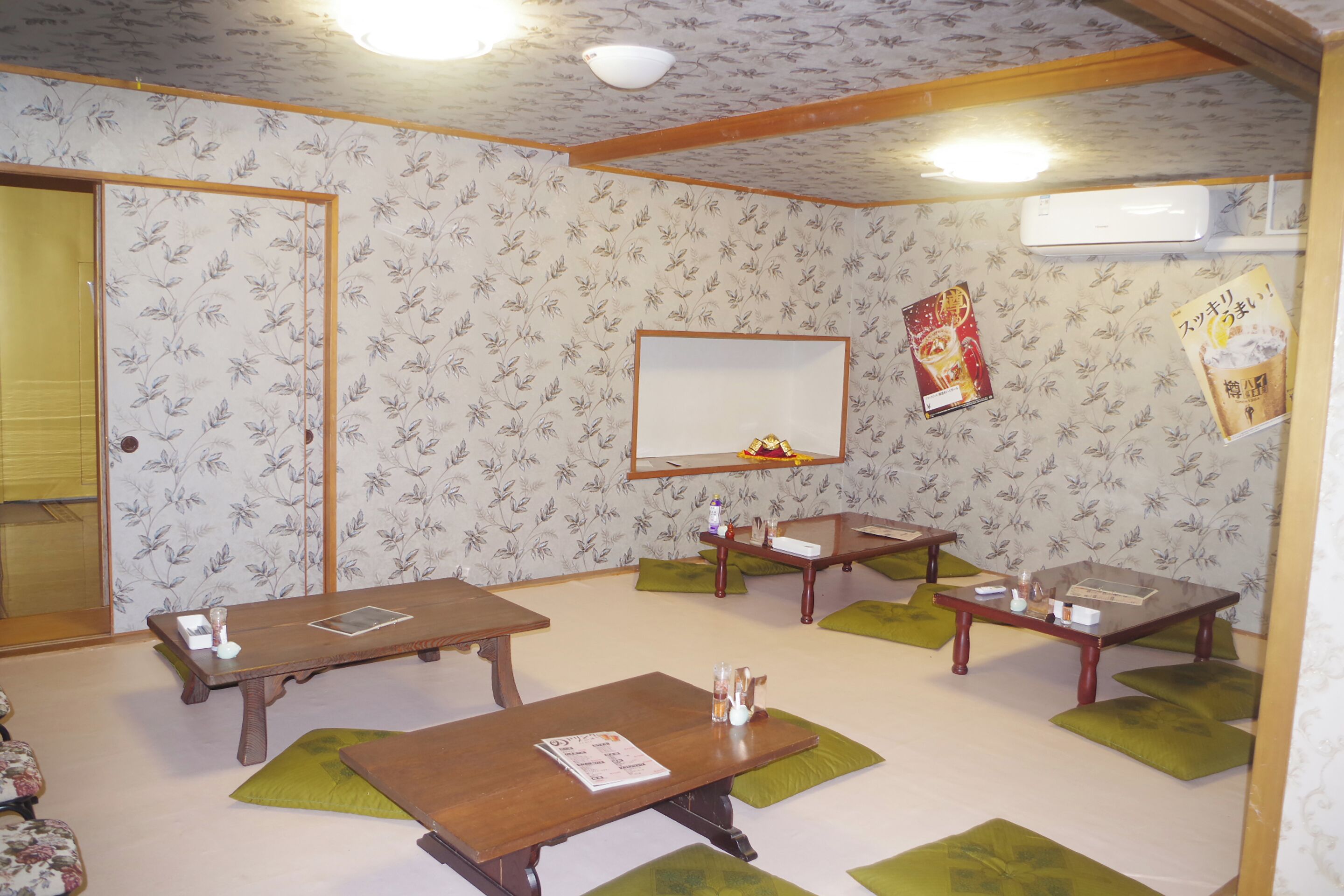 A room with four wooden tables, green cushions, a mirror, and a wall-mounted air conditioner.