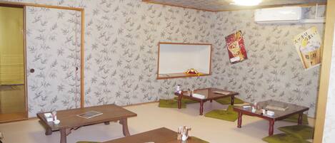 A room with four wooden tables, green cushions, a mirror, and a wall-mounted air conditioner.