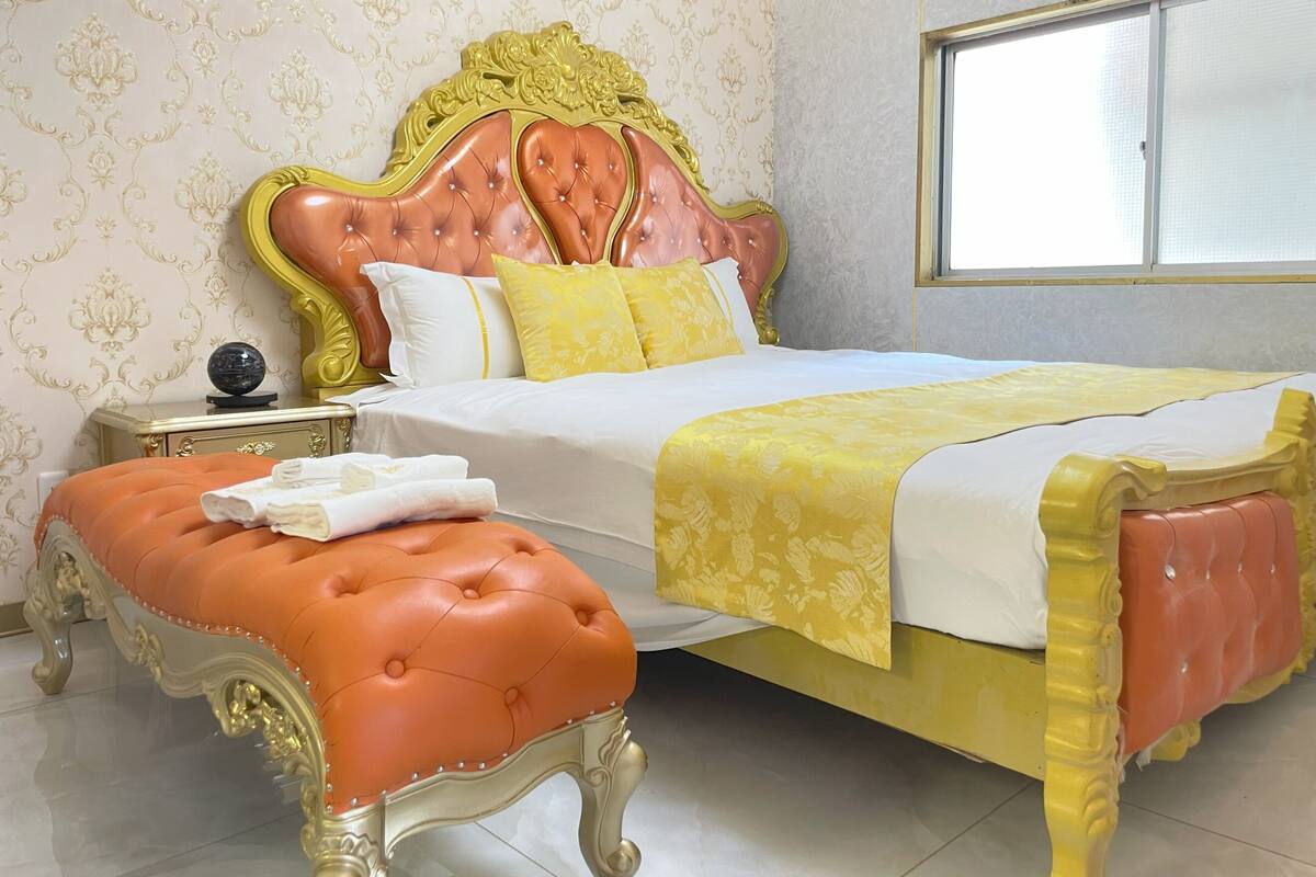 A bedroom with a large bed, ornate headboard, and a matching ottoman.