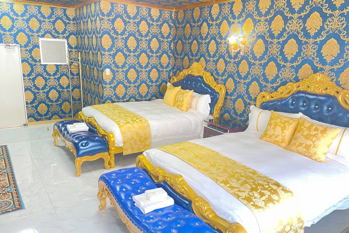 A luxurious bedroom with two beds, ornate gold and blue wallpaper, and a polished floor.