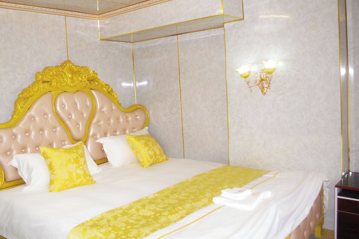 A bed with a tufted headboard, two pillows, and a yellow bedspread.