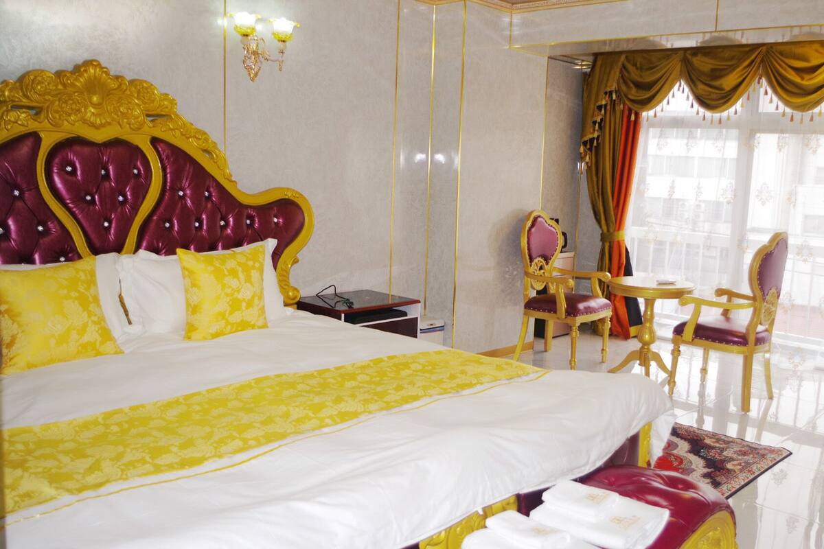 A hotel room with a large bed, a desk, two chairs, and a window with curtains.