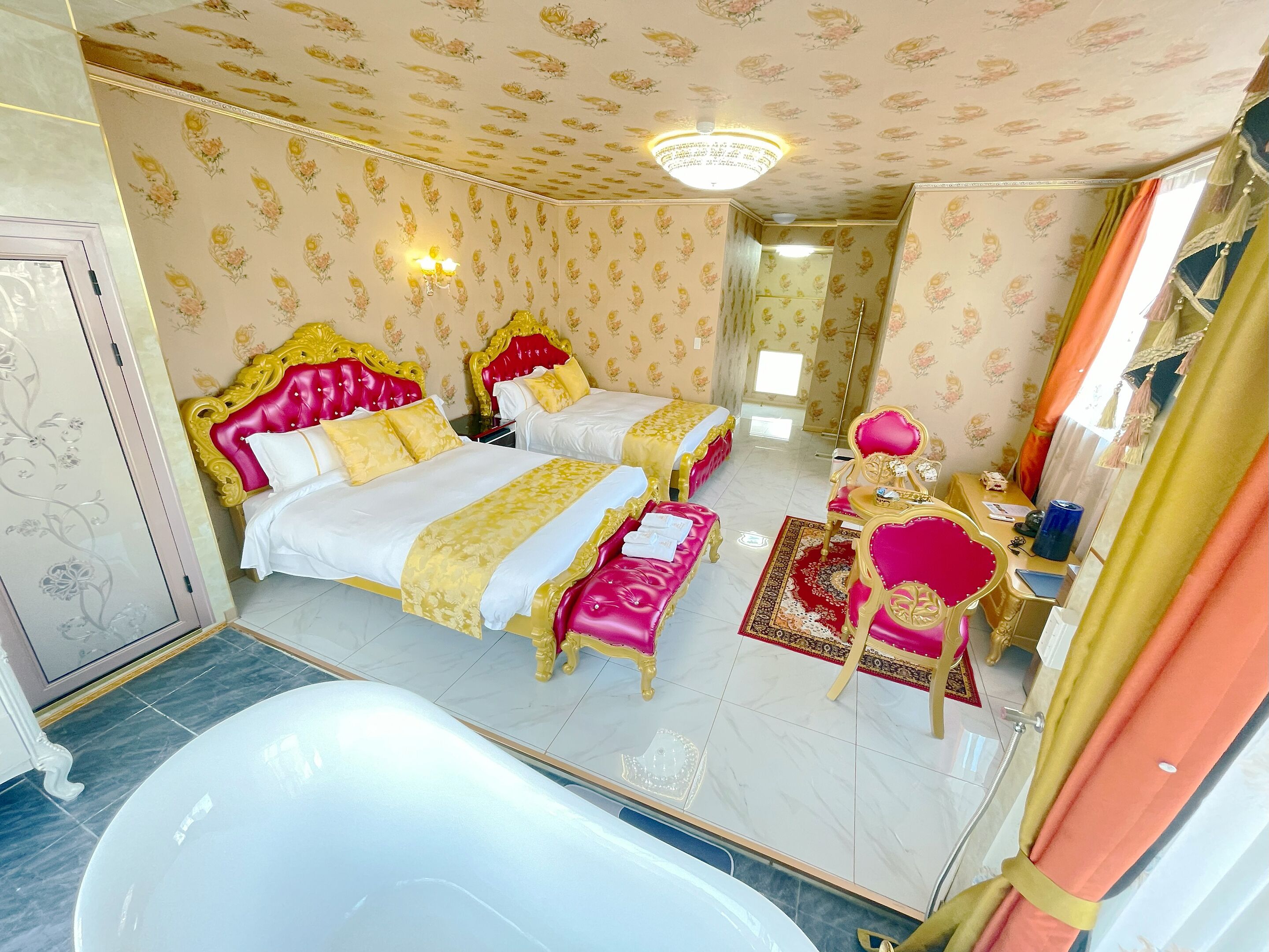 A luxurious bedroom with two beds, a vanity, and a bathtub.