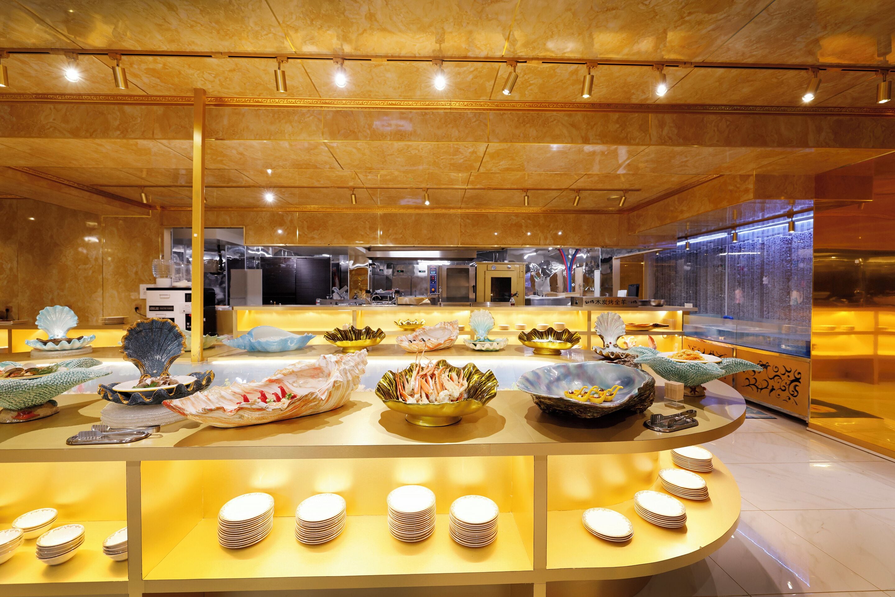 Un espace buffet proposant divers plats et assortiments de vaisselle, une cuisine en arrière-plan et un plafond en bois poli.