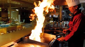 Un chef realiza una flambé con una llama grande en una cocina profesional.
