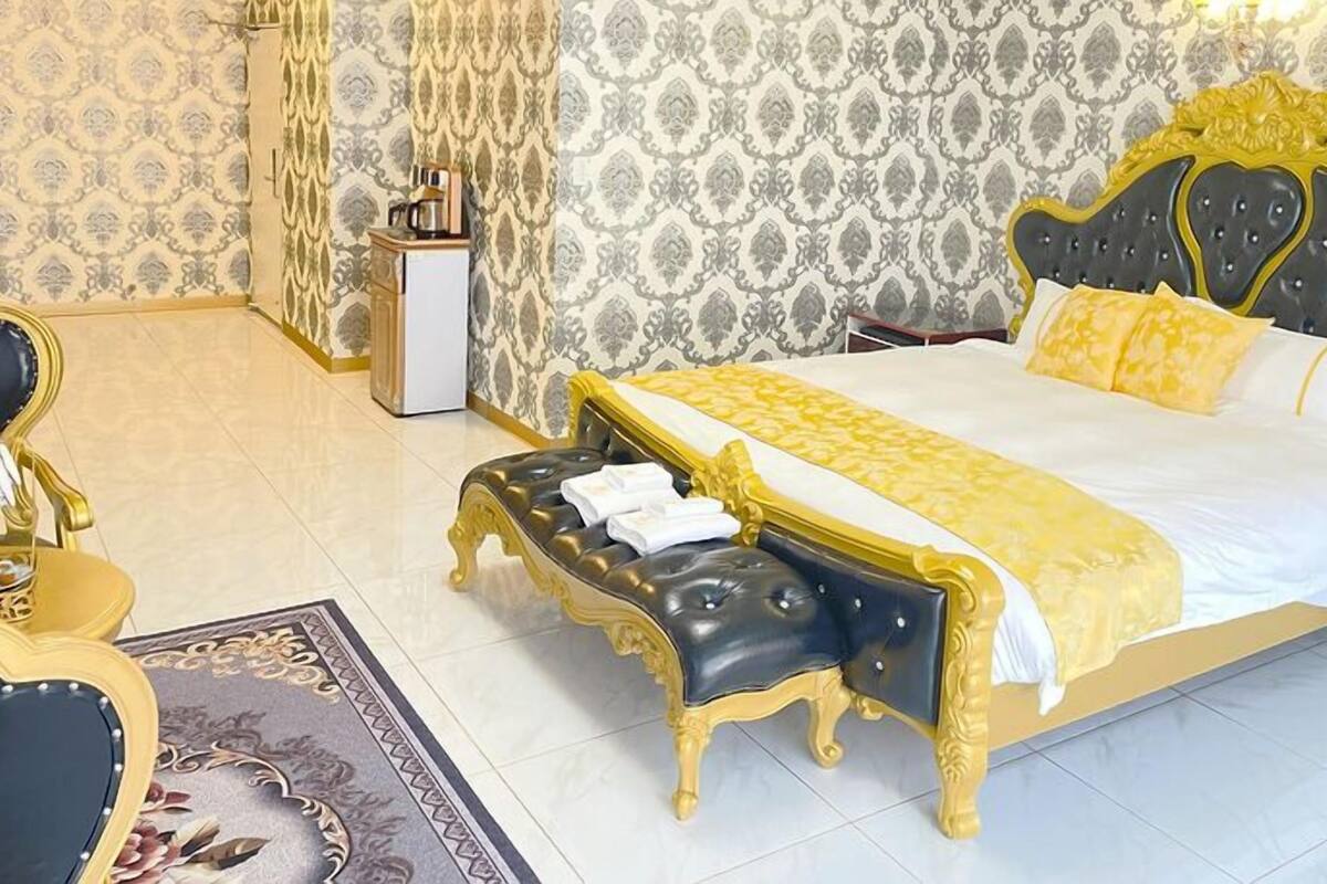 A bedroom with a large bed, a bedside table, a chair, and a small table with a coffee maker.