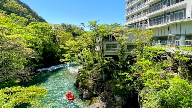 Un río con una balsa roja, rodeado de exuberante vegetación y un edificio con balcones.