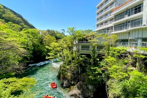 Un río con una balsa roja, rodeado de exuberante vegetación y un edificio con balcones.