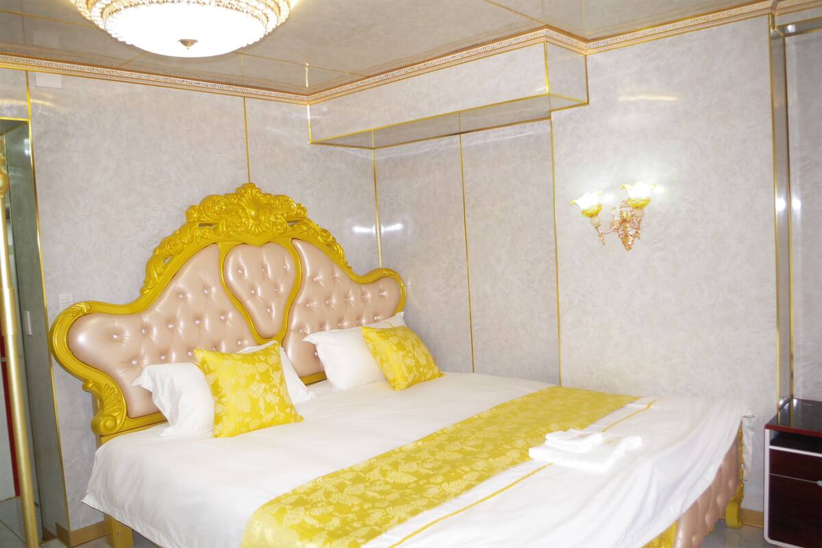 A luxurious bed with a tufted headboard, white and yellow bedding, and a decorative gold trim.