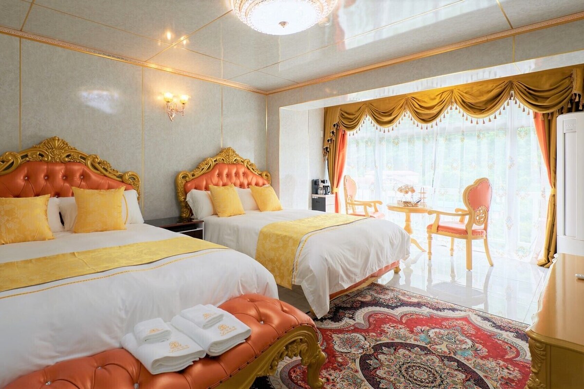 A hotel room with two beds, a dining area, and a view of the outdoors.