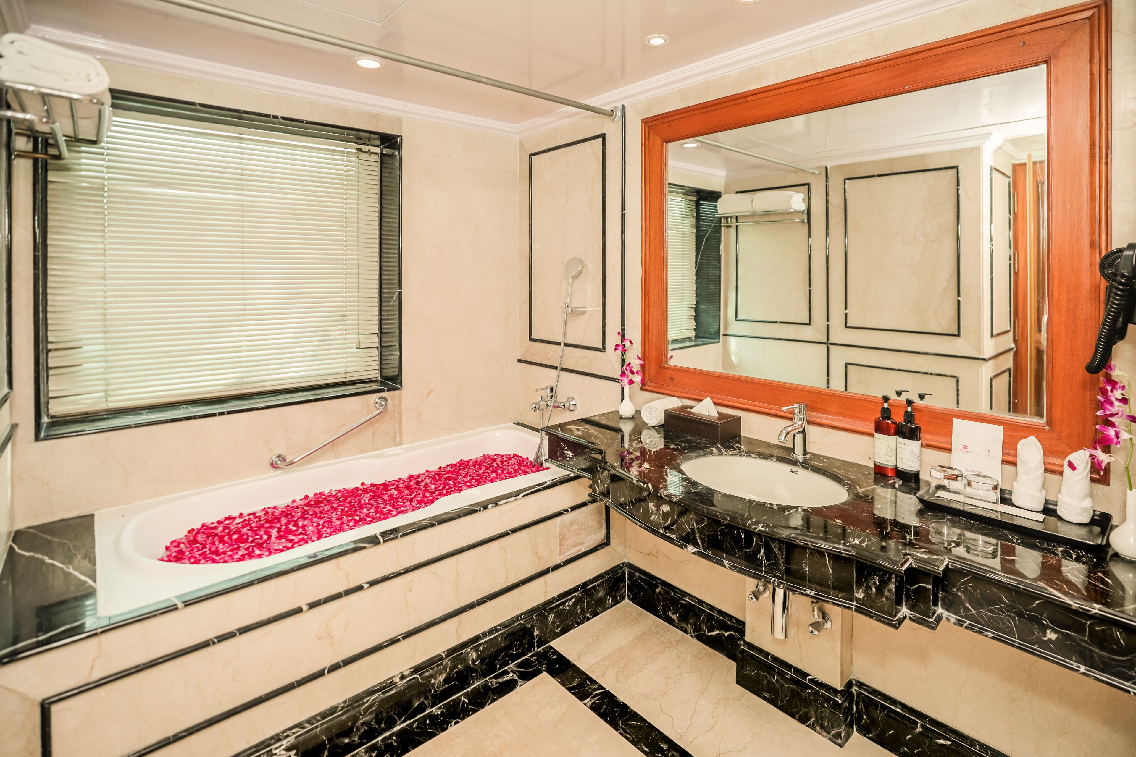 Ein modernes Badezimmer mit einer Badewanne, gefüllt mit Rosenblättern, einem großen Spiegel und einem Waschtisch mit Spüle und Pflegeprodukten.