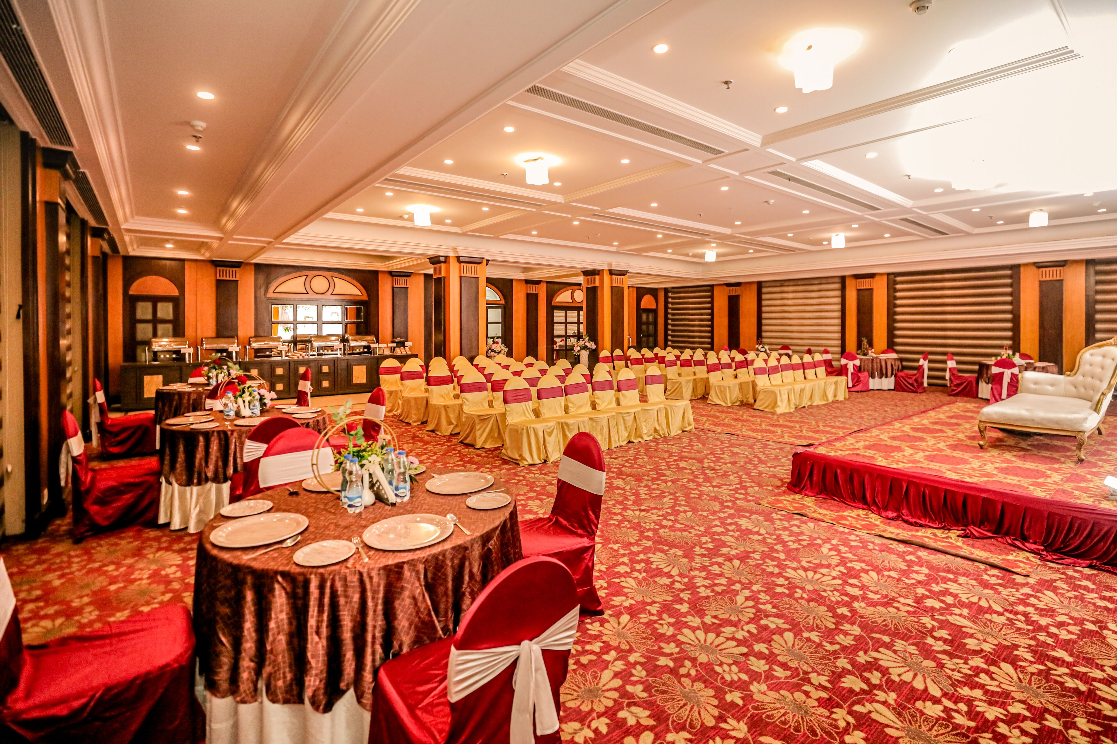 A banquet hall with round tables, red and white chairs, and a stage with a red carpet.
