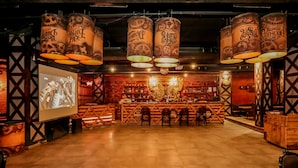 A bar area with wooden furniture, a large screen, and decorative hanging lamps. - Regenta Central Lucknow by Royal Orchid Hotels Limited (Lucknow)
