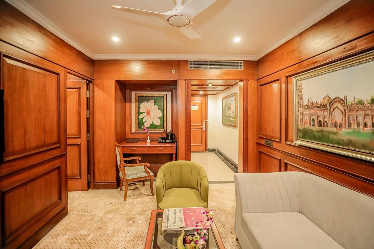 A room with wooden paneling, a desk with a chair, a sofa, a ceiling fan, and a large framed picture on the wall.