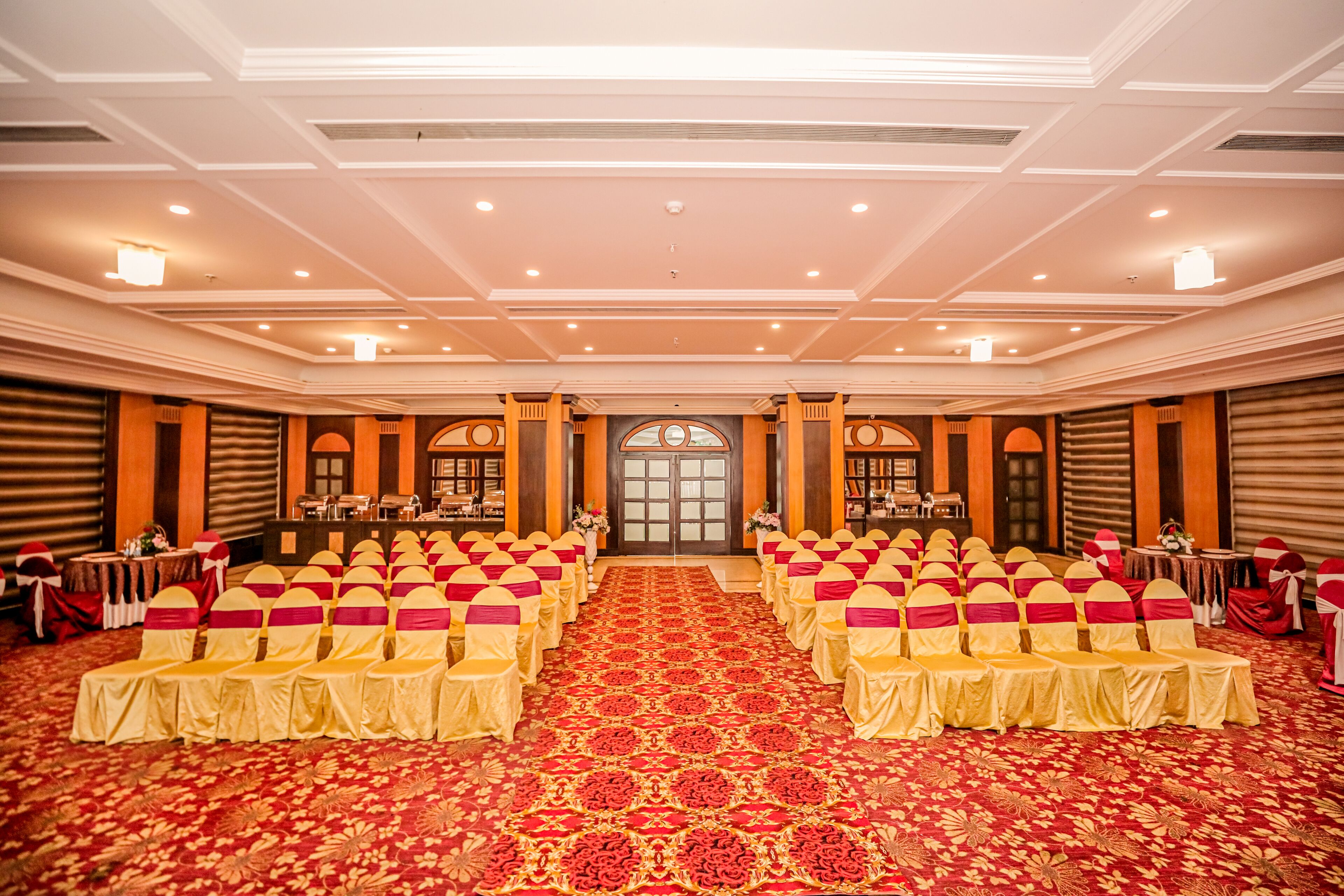 A banquet hall with rows of tables and chairs, a patterned carpet, and a large arched doorway.