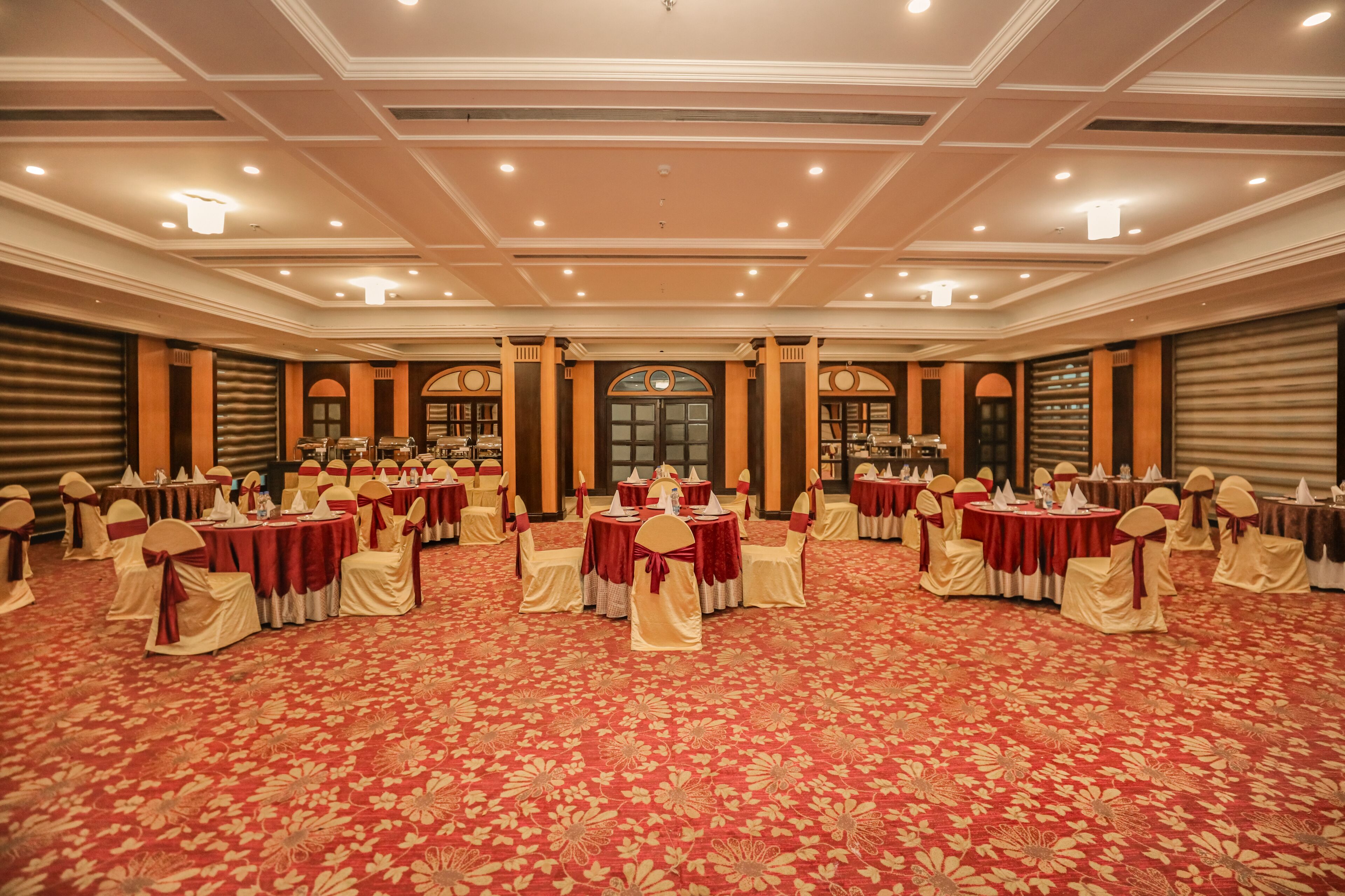 Un salón de banquetes con mesas redondas dispuestas en forma de U, cada una con mantel rojo y sillas blancas.