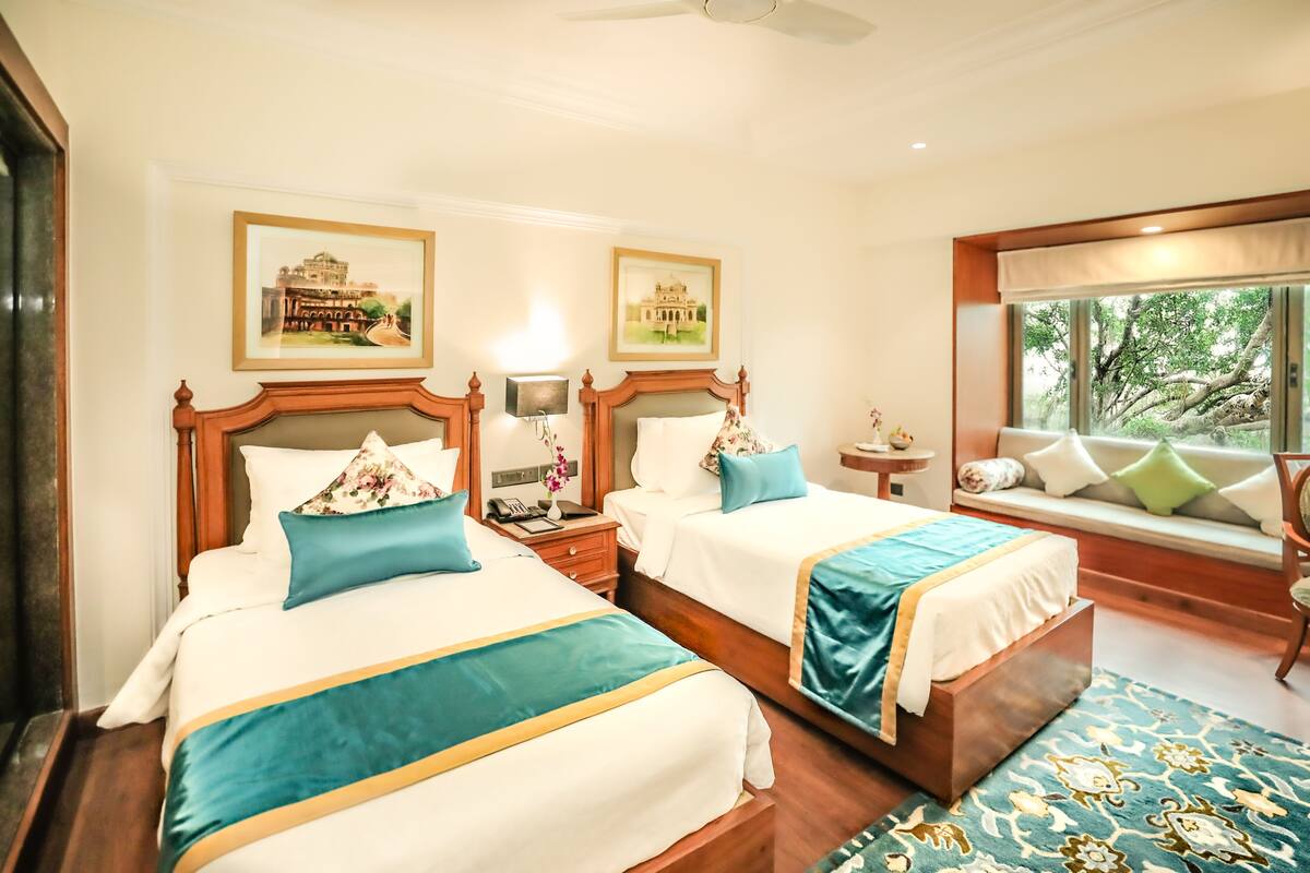 A hotel room with two beds, a window seat, and artwork on the walls.