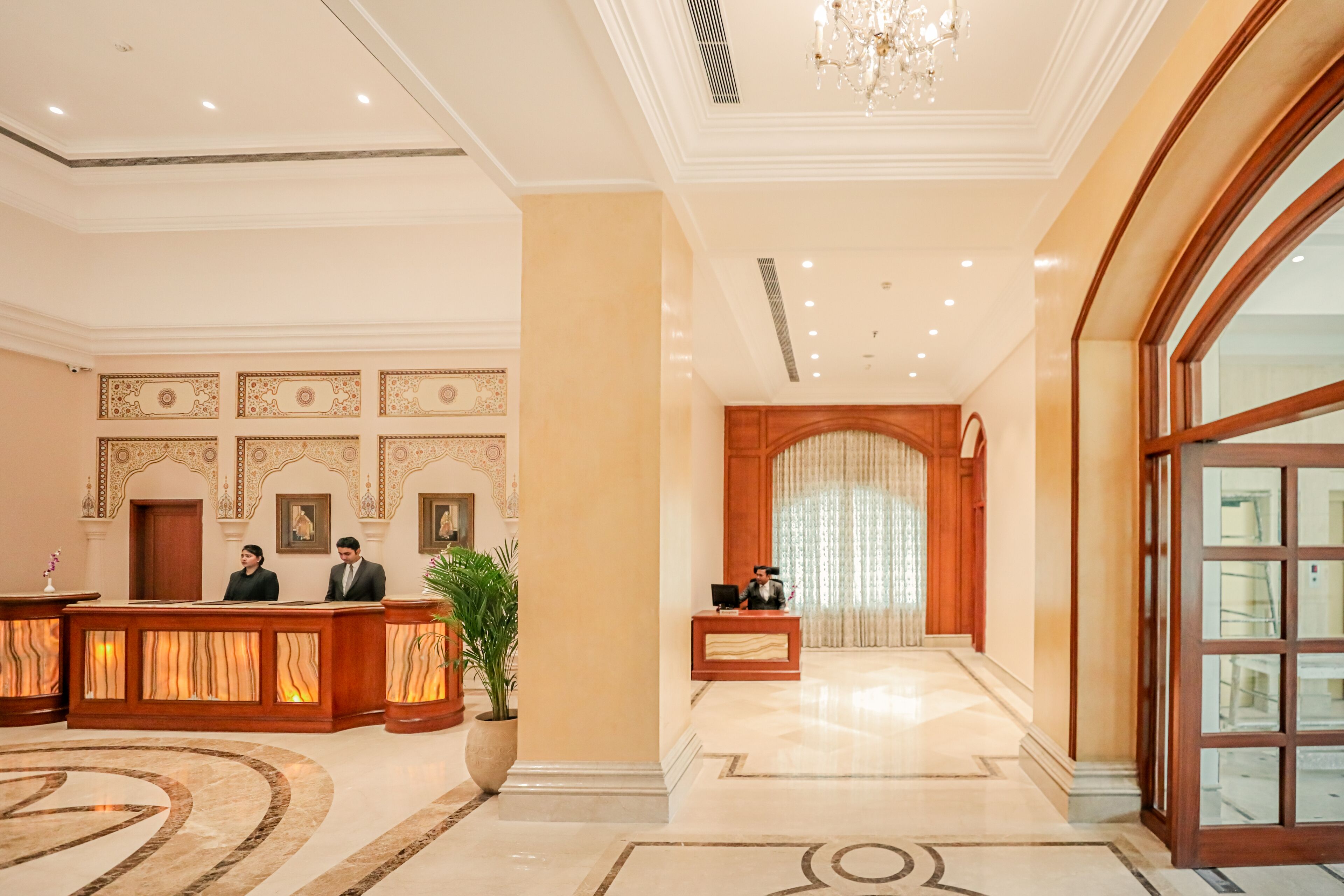 Eine Hotellobby mit einer Rezeption, einer großen Topfpflanze und einem prunkvollen Kronleuchter.
