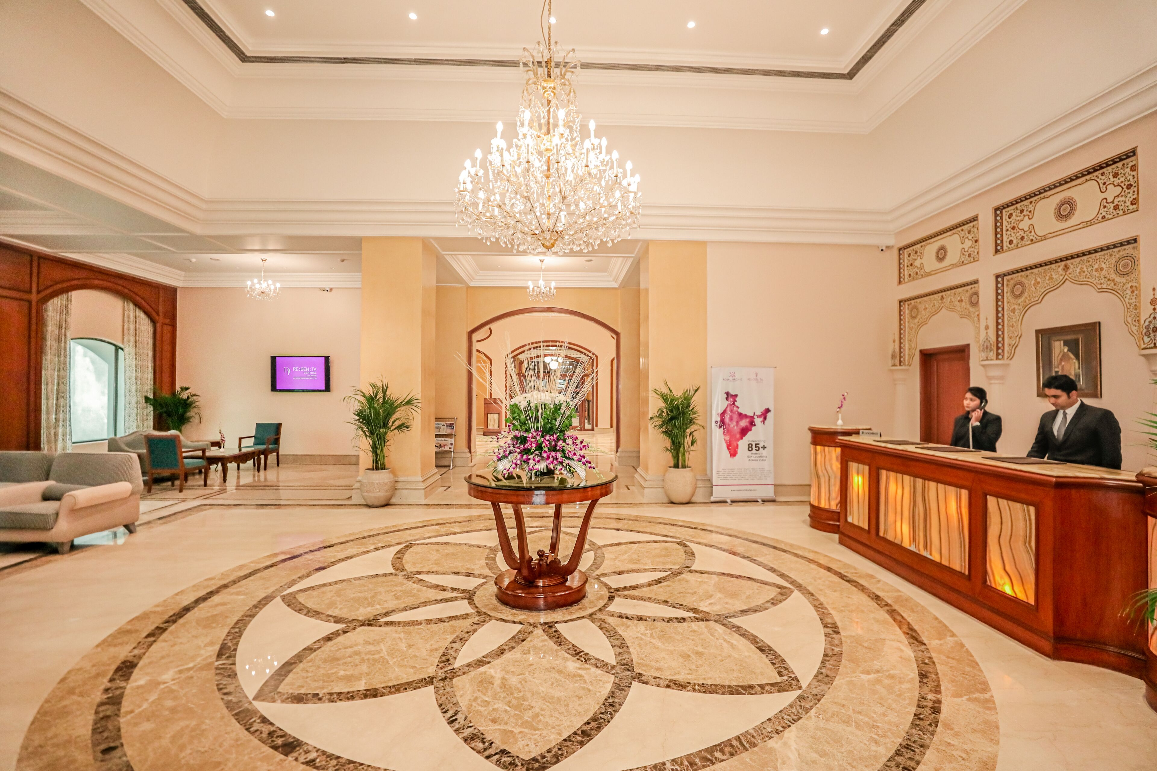 A hotel lobby with a grand chandelier, a reception desk, and a decorative floor pattern.