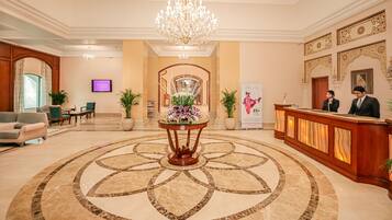 A hotel lobby with a grand chandelier, a reception desk, and a decorative floor pattern.