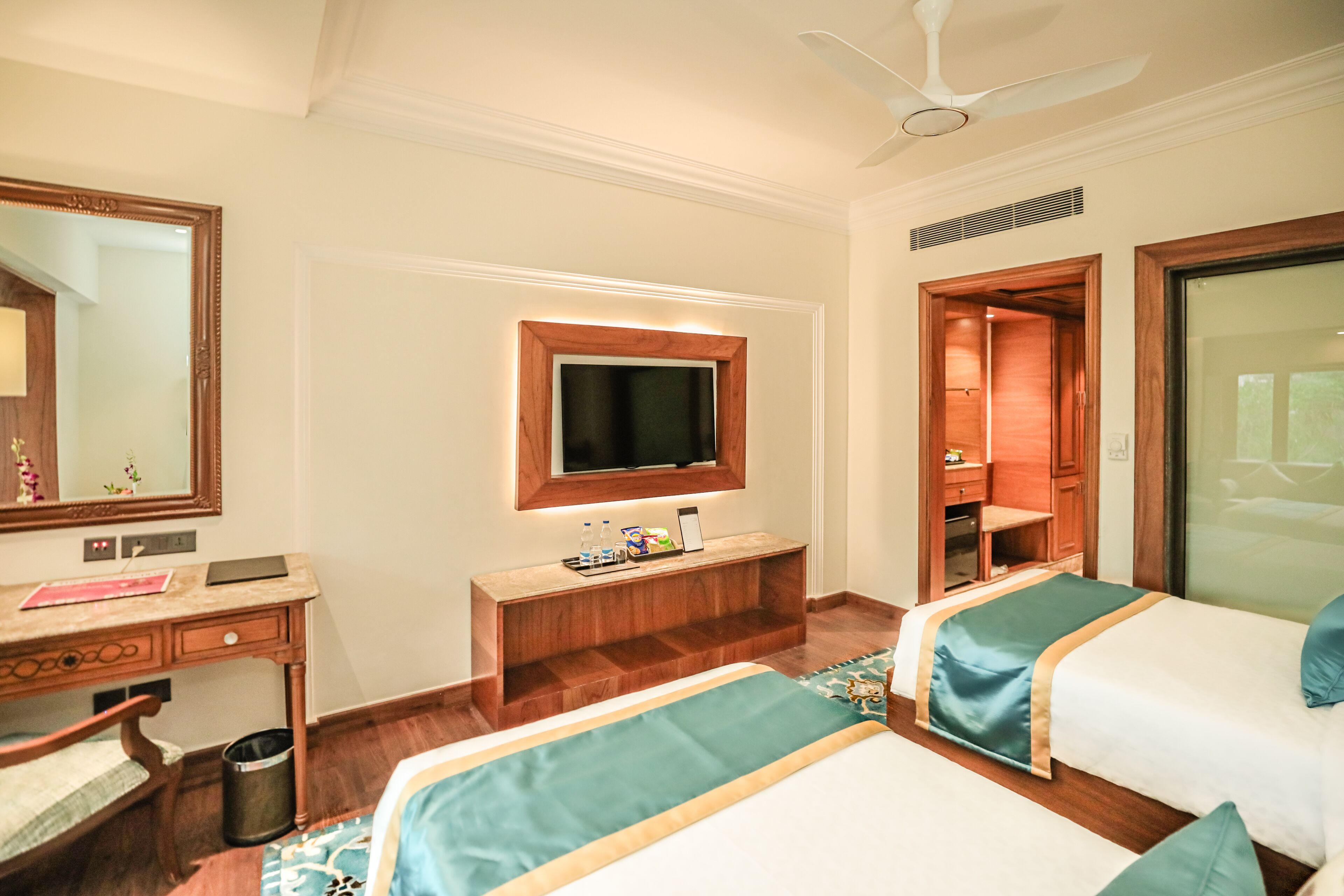 A hotel room with two beds, a desk, a mirror, a television, and a wardrobe.