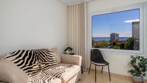 Un salón moderno con un sofá color beige, un sillón negro y un ventanal con vistas al mar y edificios.