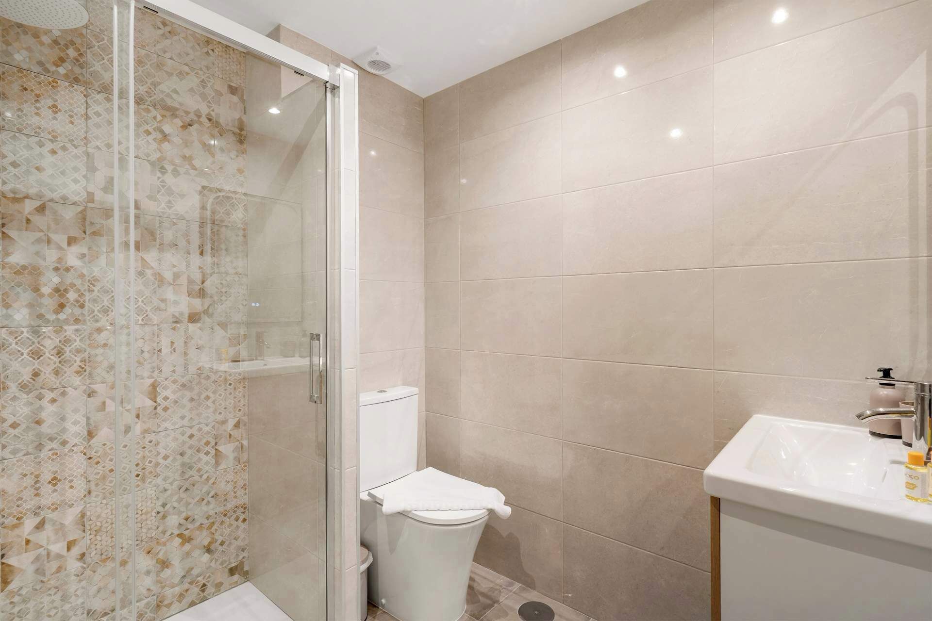 A bathroom with a glass shower enclosure, a toilet, and a sink with a soap dispenser.