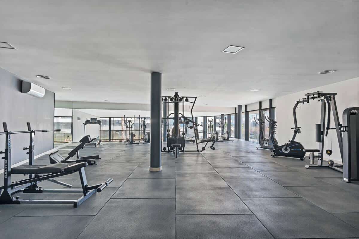 Un gimnasio amplio con diversos equipos de ejercicio, ventanas grandes y un diseño moderno y limpio.