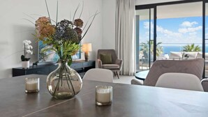 Una habitación de hotel moderna con una mesa de comedor, un jarrón con flores y vista al océano.