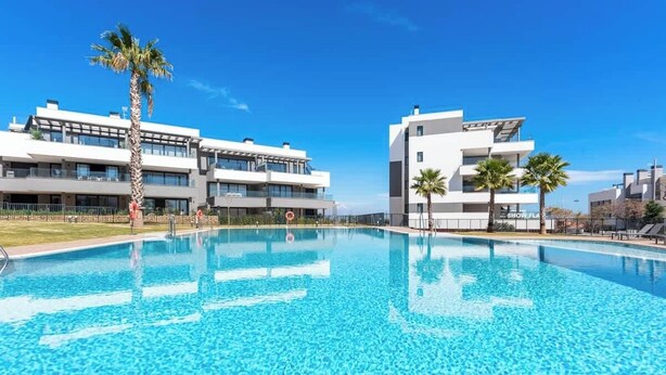 Un hotel moderno con piscina, palmeras y un cielo azul despejado.