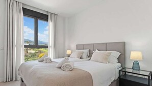 Habitación de hotel moderna con una cama grande, dos mesitas de noche y vistas al exterior.