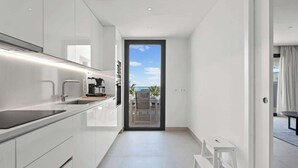 Una cocina moderna con armarios blancos, encimera negra y cafetera. Hay una puerta corrediza de vidrio que da a un área exterior con una mesa y sillas.