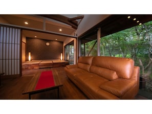 A modern interior with a leather sofa, wooden flooring, a red rug, and a traditional Japanese screen.