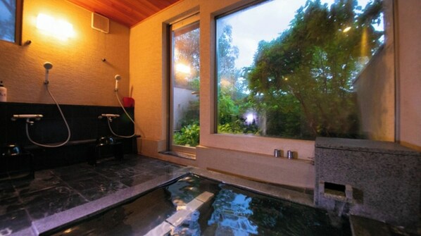 A bathroom with a glass-enclosed hot tub, a shower, and a window with a view of greenery.