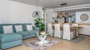 A modern living room with a teal sofa, glass coffee table, and dining area with white chairs. - Exclusive Seaview Apt by Costarentals - Ref 02 (Fuengirola)