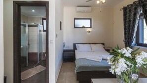 A bedroom with a bed, a bedside table, a nightstand, a mirror, a ceiling fan, and a window with curtains. - Fegaropetra studios (Igoumenitsa)