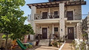 A two-story stone building with a balcony on the upper floor, a small garden area with potted plants, and a red toy car on the ground. - Fegaropetra studios (Igoumenitsa)