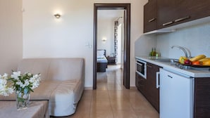 A compact living space with a kitchenette, a sofa, and a bedside table with a vase of flowers. - Fegaropetra studios (Igoumenitsa)